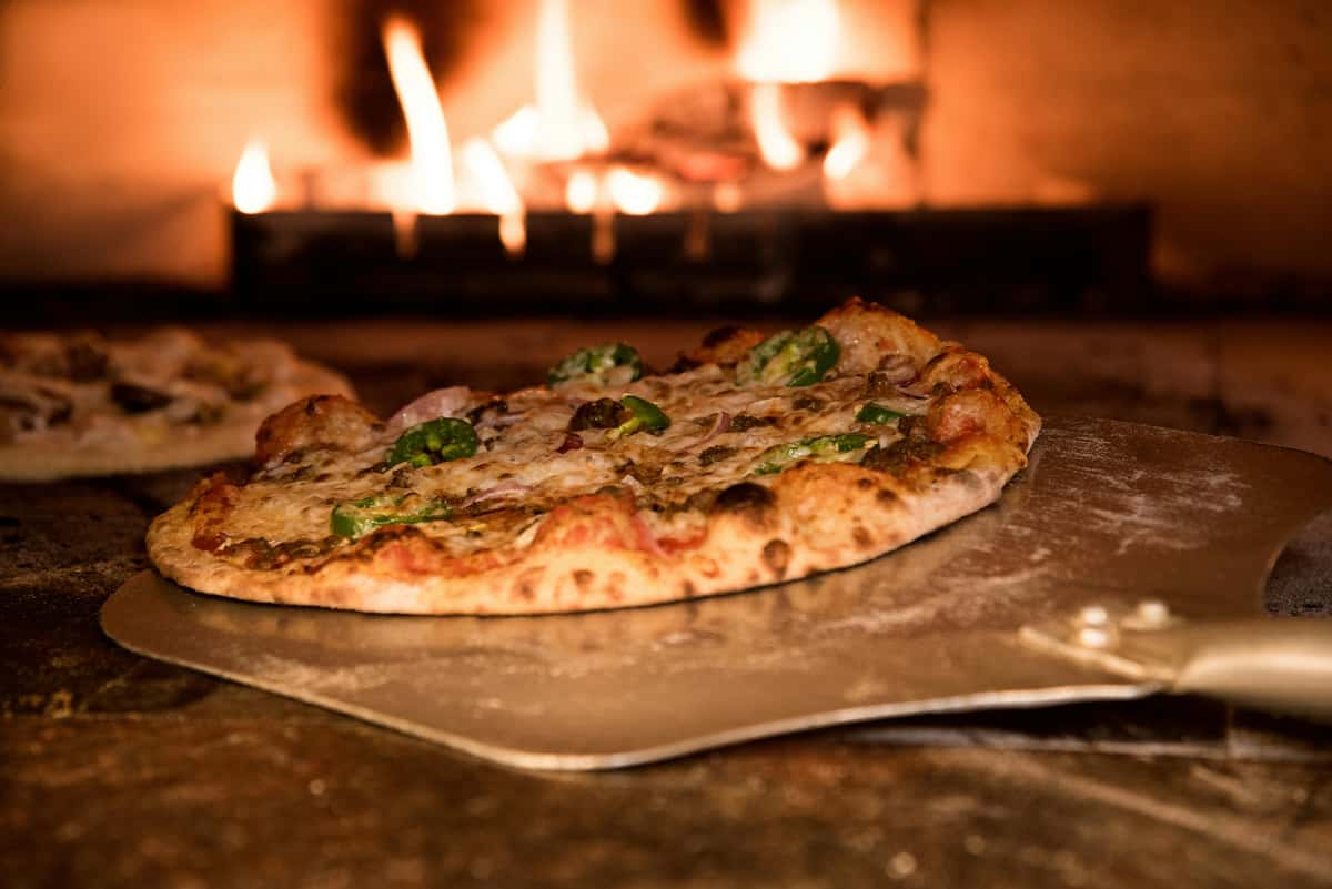 Freshly baked wood-fired pizza with melted cheese and jalapeño slices being pulled from a brick oven at Wyoming Ale Works.