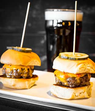 Juicy cheeseburger sliders topped with pickles on toasted buns, served with a pint of dark beer at Wyoming Ale Works.